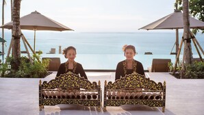 Two ornate beds with a view of the sea, surrounded by palm trees and umbrellas. - Novotel Bali Benoa (Nusa Dua)