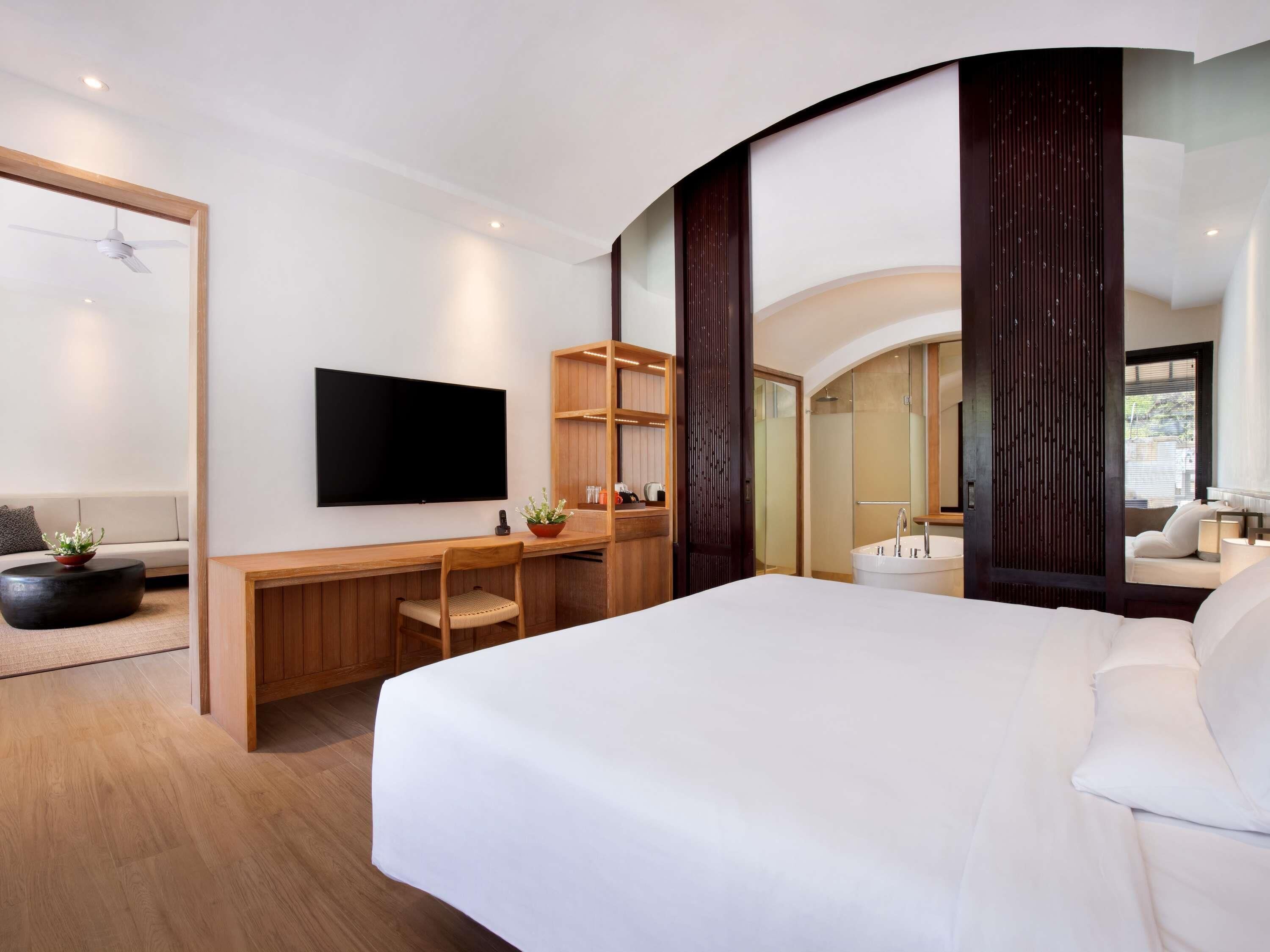 Une chambre d’hôtel moderne dotée d’un grand lit, d’un téléviseur à écran plat, d’un bureau avec une chaise, d’une plante en pot et d’un espace douche.