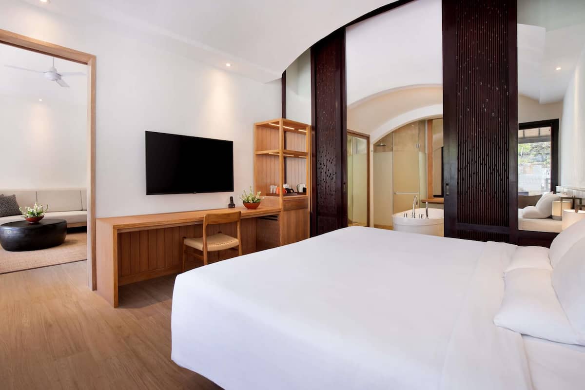 Une chambre d’hôtel moderne dotée d’un grand lit, d’un téléviseur à écran plat, d’un bureau avec une chaise, d’une plante en pot et d’un espace douche.