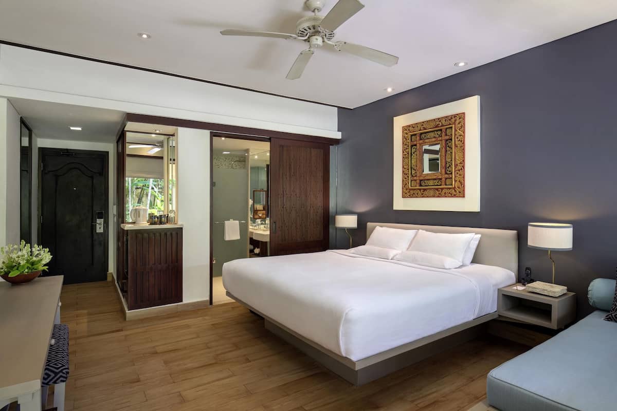 Une chambre à coucher moderne avec un grand lit, des tables de chevet, un ventilateur de plafond et un miroir décoratif.