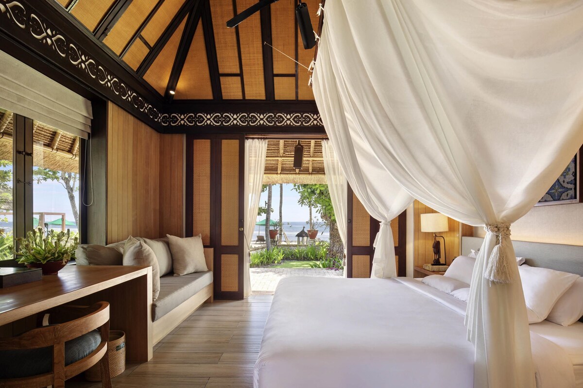 A room with a bed, a sofa, a wooden desk, and a view of the ocean.