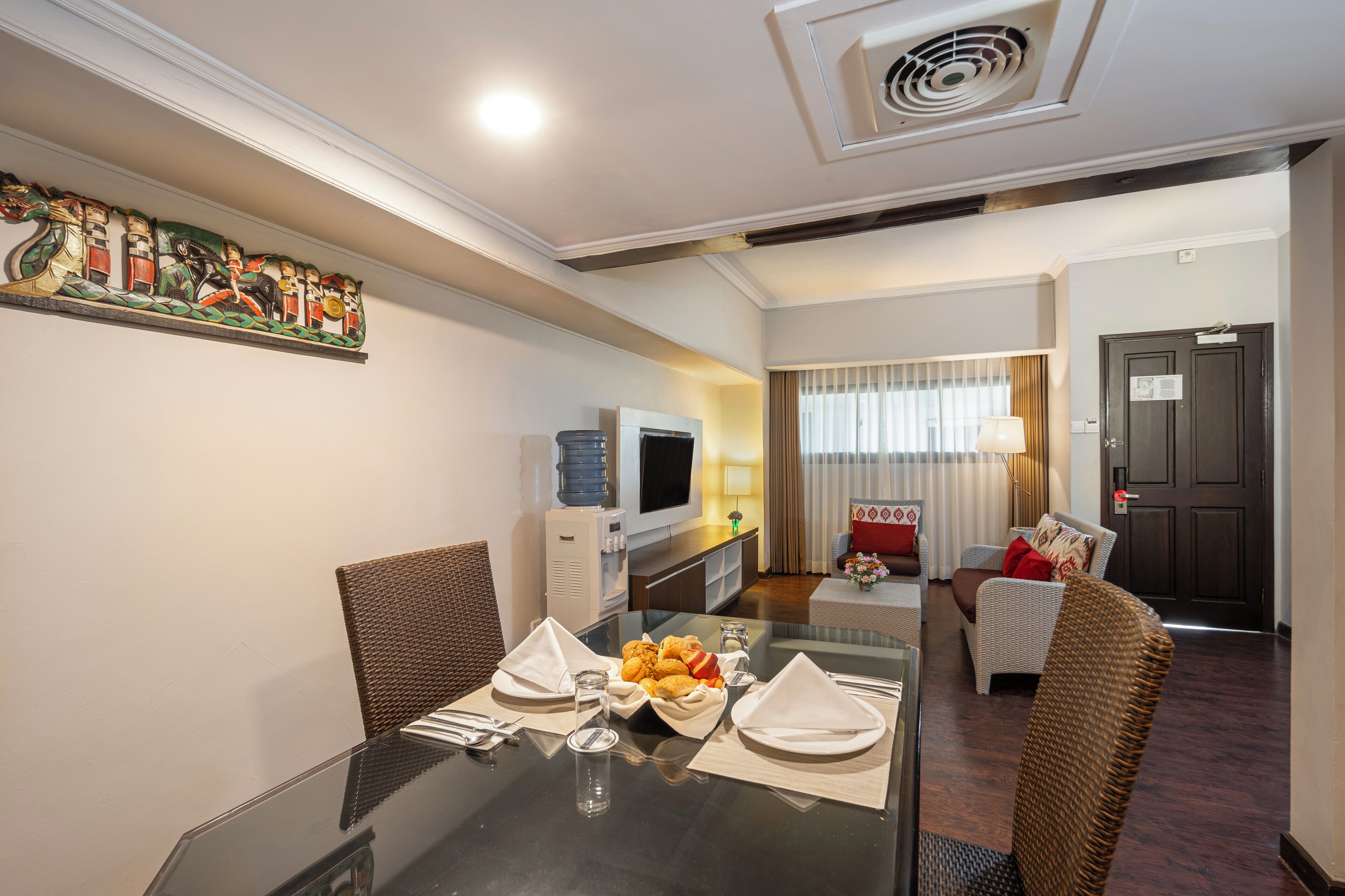 Une chambre d’hôtel équipée d’une table à manger pour deux personnes, d’une télévision, d’un distributeur d’eau et d’un canapé dans l’espace salon.