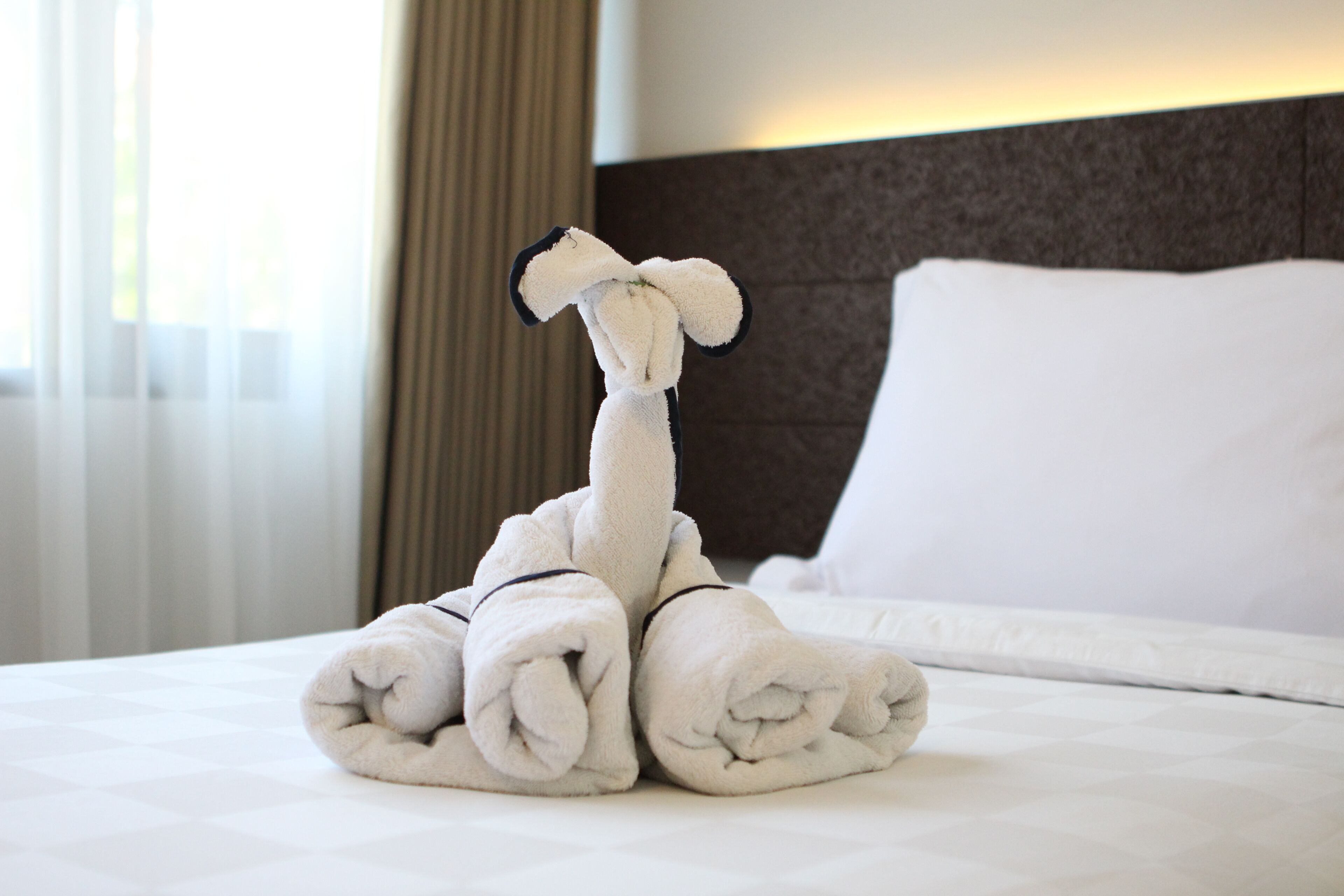 A neatly made bed with a towel sculpture resembling a giraffe, a white pillow, and a headboard.