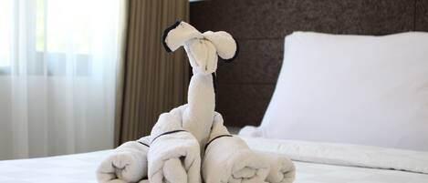 A neatly made bed with a towel sculpture resembling a giraffe, a white pillow, and a headboard.