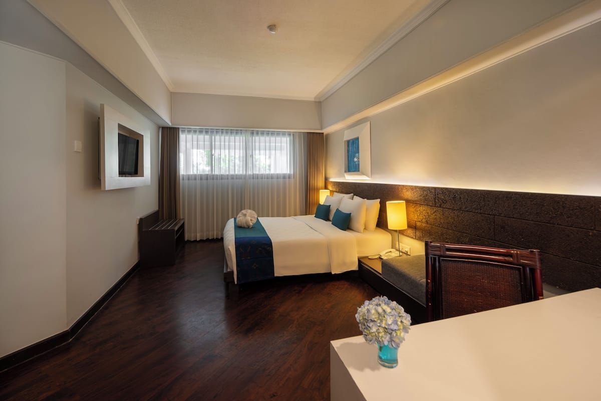 A hotel room with a bed, bedside table, lamp, and a small table with a vase.