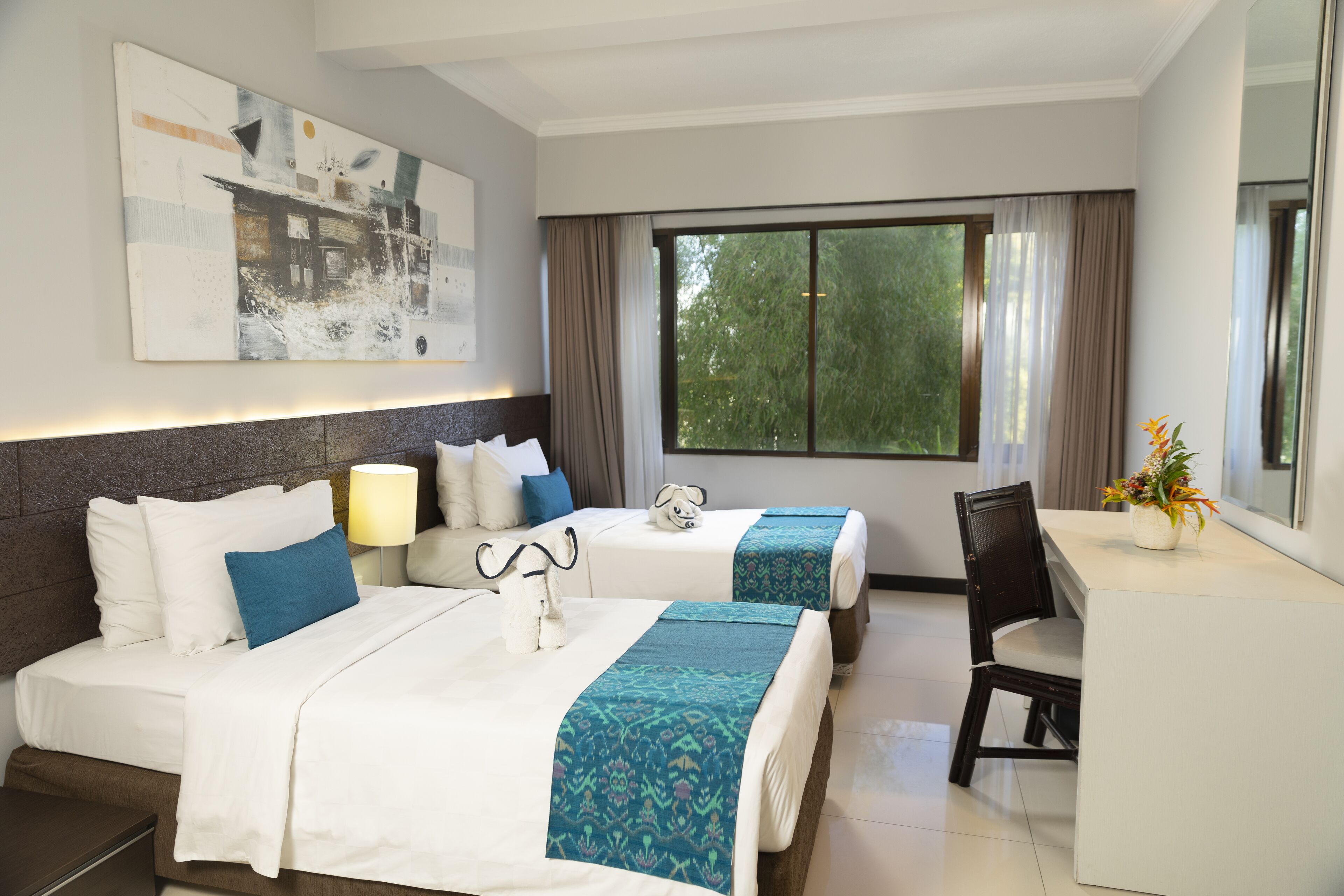 A hotel room with two beds, a desk, and a large window.