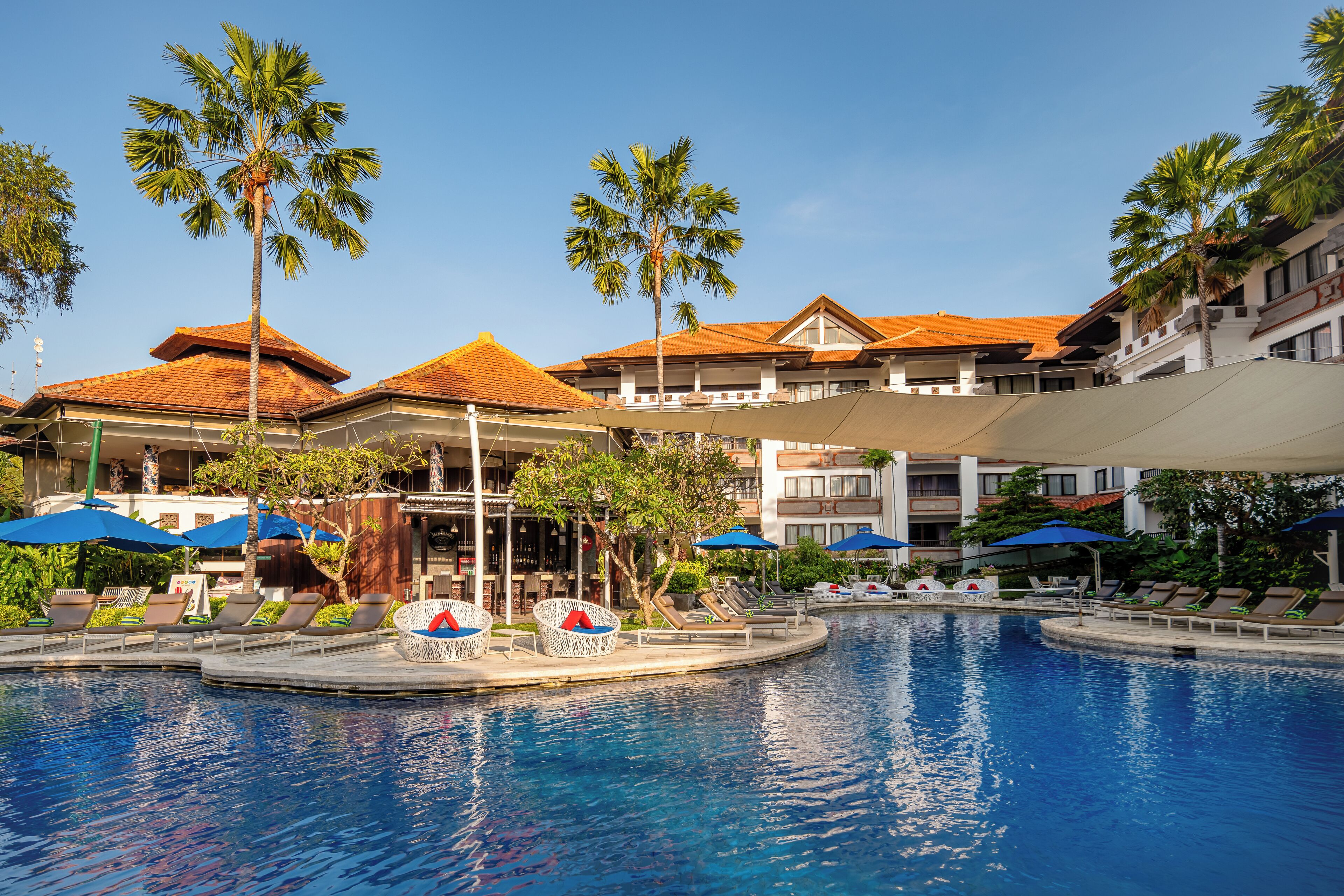 Een zwembadgedeelte van een resort met palmbomen, ligbedden en parasols.