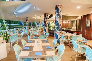 An indoor restaurant with multiple tables and chairs, a bar area, and tropical-themed columns. - Prime Plaza Suites Sanur - Bali (Denpasar)