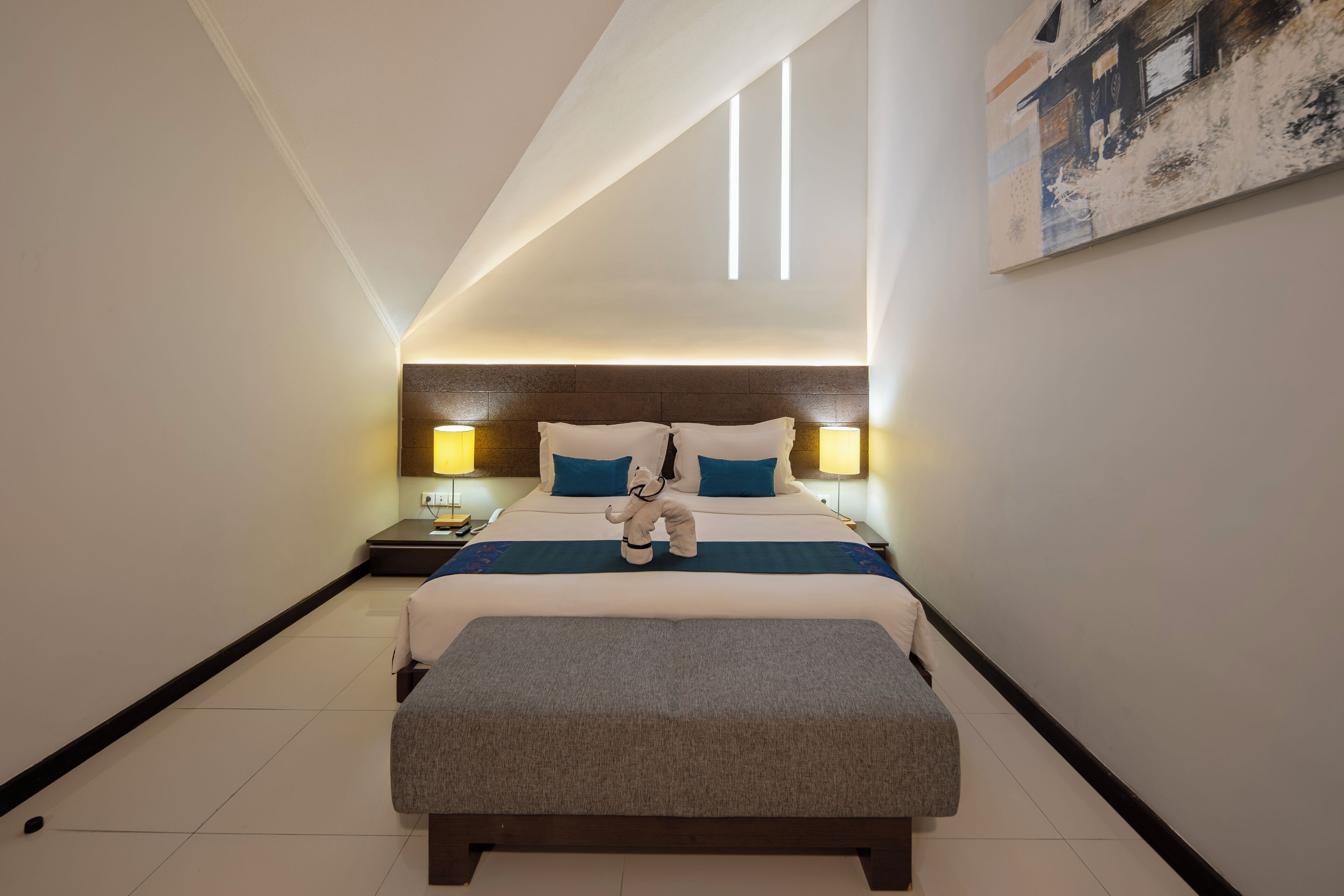 A hotel room with a large bed, bedside lamps, a nightstand, and a wall-mounted painting.