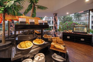 A buffet with various food items, including pancakes and pastries, in a well-lit indoor setting with a view of a building outside. - Prime Plaza Suites Sanur - Bali (Denpasar)