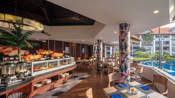 Un restaurante con bufé, suelo de madera y vistas a una piscina y un edificio al fondo.