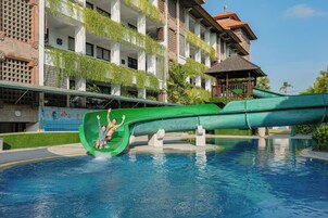 A swimming pool with a green water slide and a building with balconies in the background.
