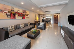 A modern living room with a sofa set, a coffee table with flowers, a TV, and a kitchen area in the background.