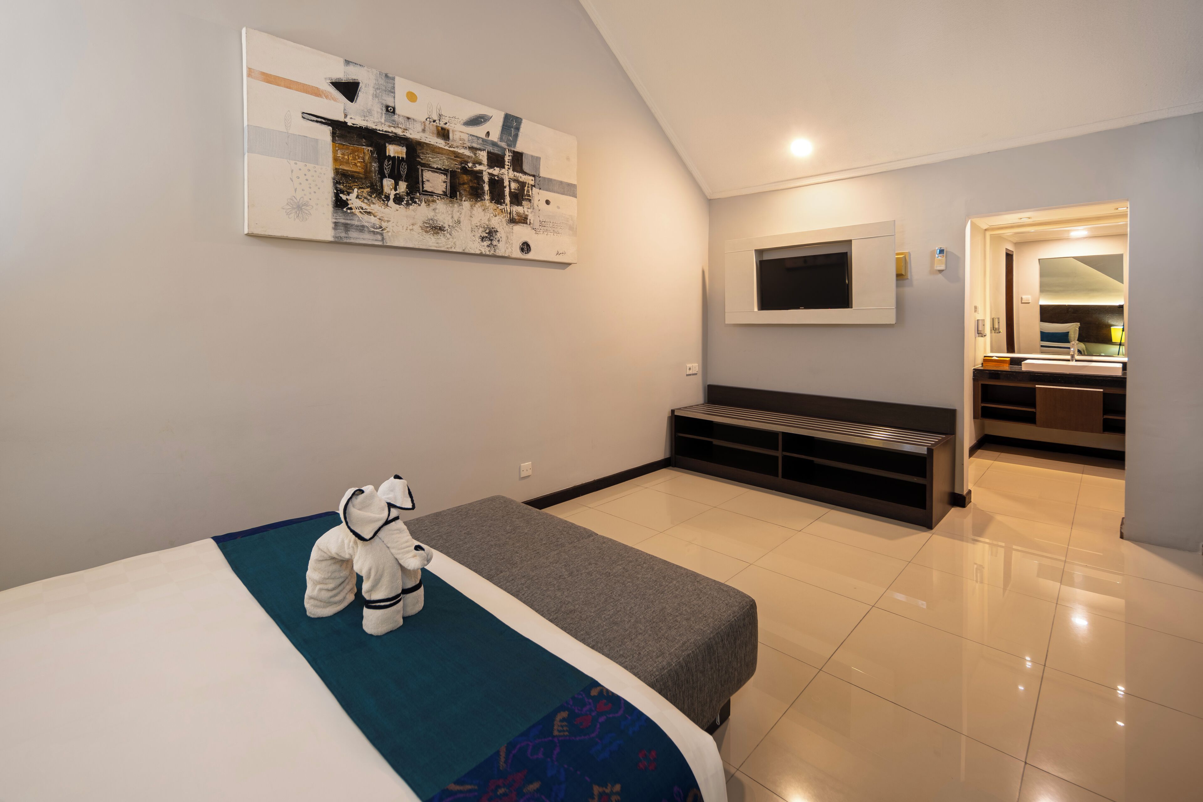 Een hotelkamer met een bed, een bankje, een aan de muur bevestigde televisie en een kleine kitchenette.
