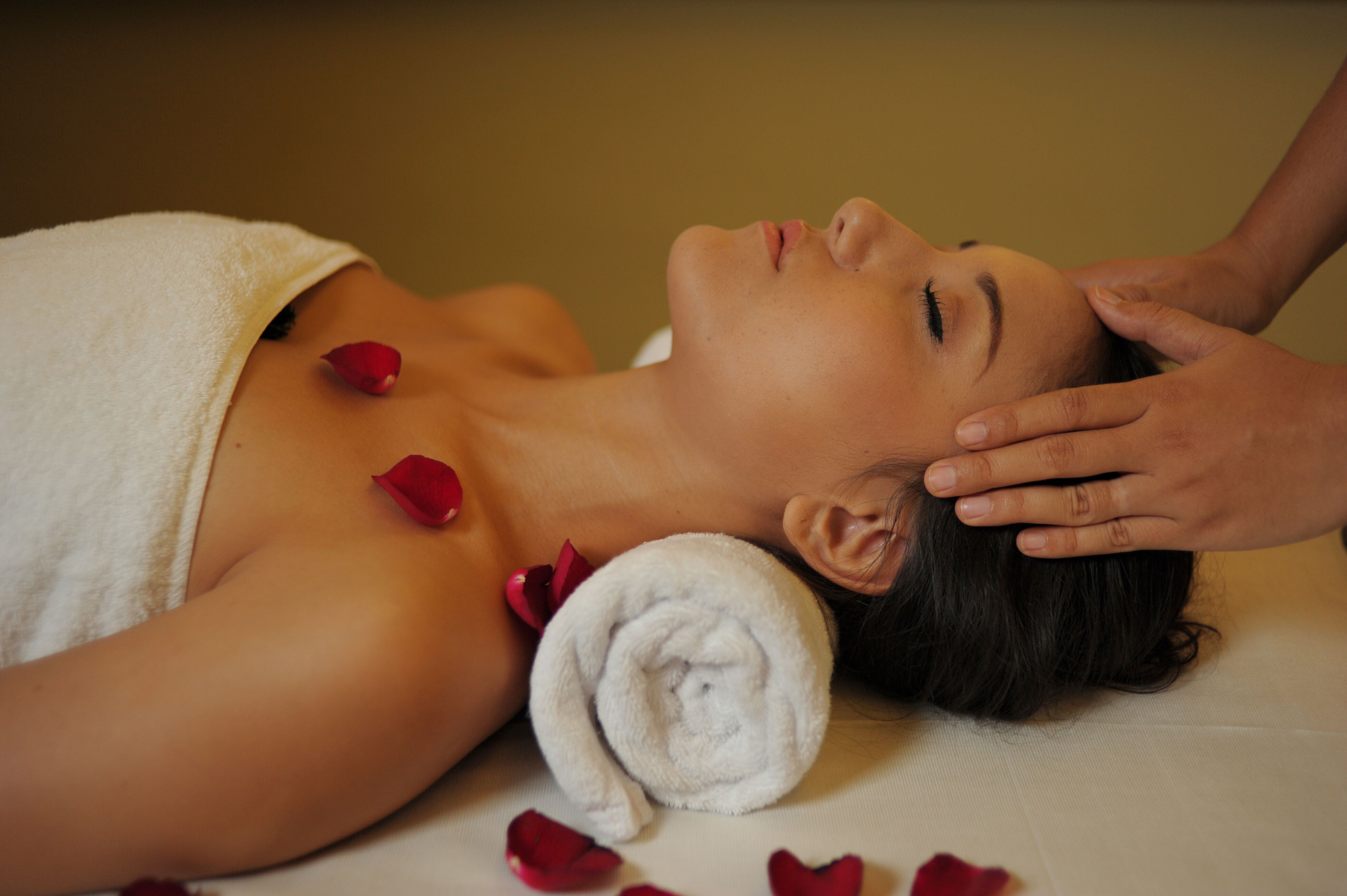 A person lying down with a towel wrapped around their neck and a rolled towel beside them.