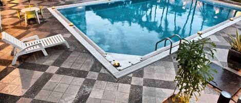 Een rechthoekig zwembad met betegeld zonneterras, omringd door ligbedden en parasols, en een kleine hottub.