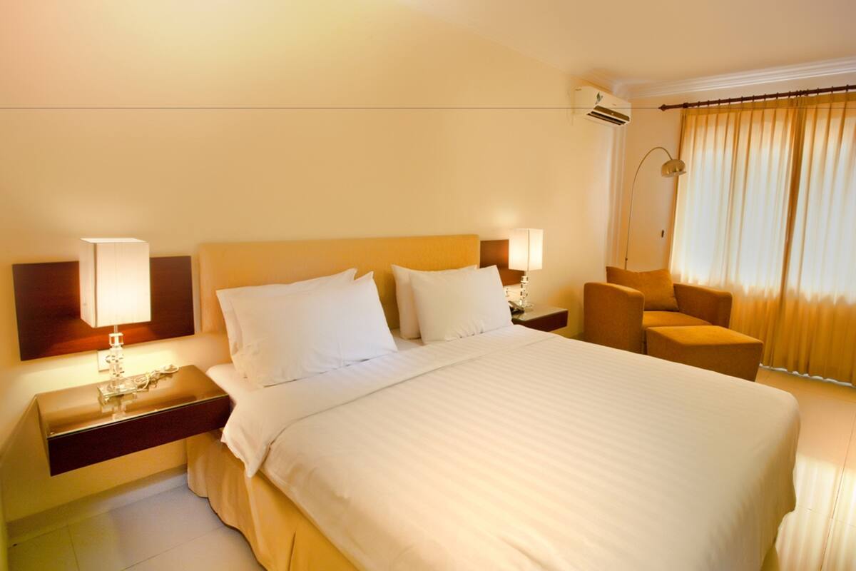 A hotel room with a large bed, bedside lamps, a chair, and a window with curtains.