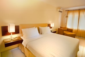 A hotel room with a large bed, bedside lamps, a chair, and a window with curtains.