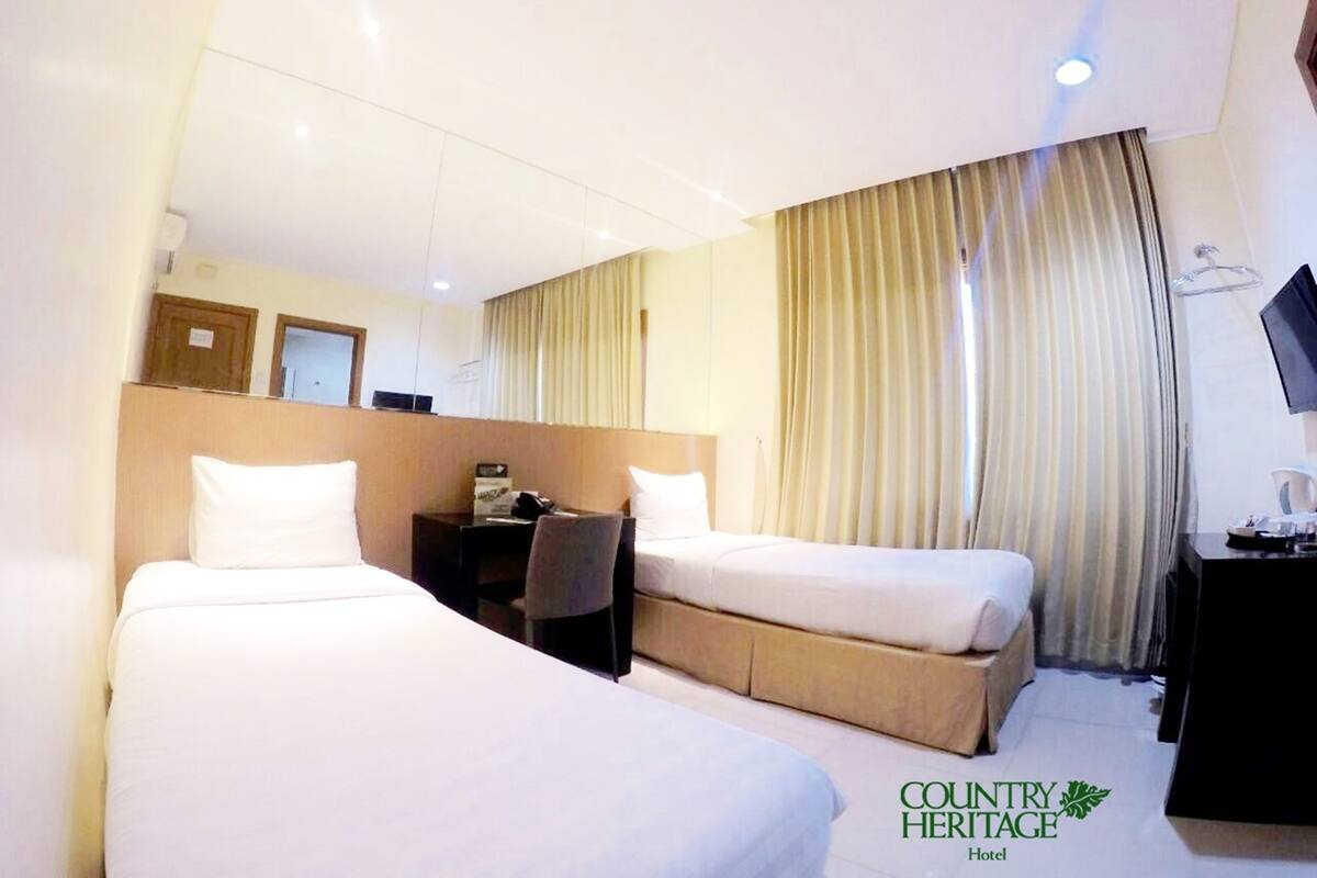 A hotel room with two beds, a desk, a chair, a television, and a window with curtains.