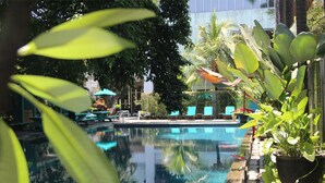 A swimming pool with lounge chairs and umbrellas, surrounded by greenery and a building in the background. - Mercure Surabaya Grand Miram (Surabaya)