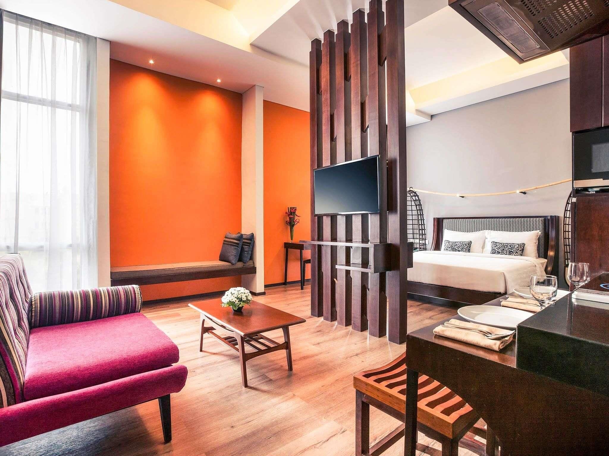 Una habitación de hotel moderna con piso de madera, un sofá, una mesa de comedor, una cama y un televisor.