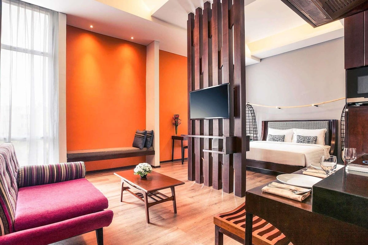 Una habitación de hotel moderna con piso de madera, un sofá, una mesa de comedor, una cama y un televisor.