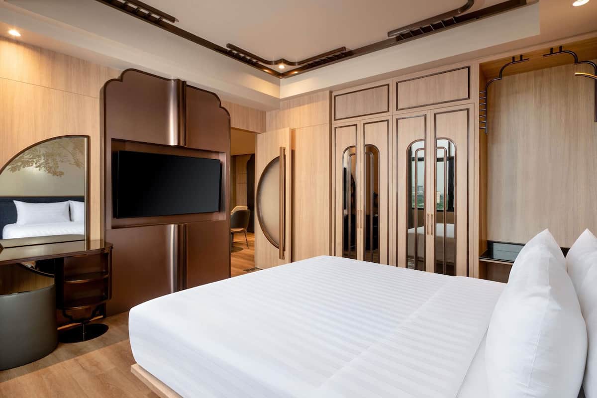 A modern hotel room with a large bed, a TV, a wardrobe with mirrors, and a seating area.