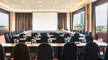 Un salón de conferencias con una pantalla grande, varias mesas y sillas dispuestas para reuniones.