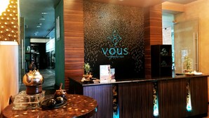 A reception area with a modern design, featuring a reception desk, a decorative wall with a logo, and a small table with a teapot and cups. - Mercure Surabaya Grand Miram (Surabaya)