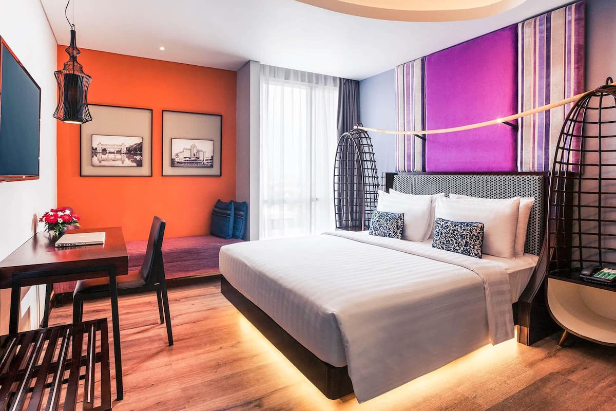 A modern hotel room with a bed, a desk, a chair, and a hanging chair.