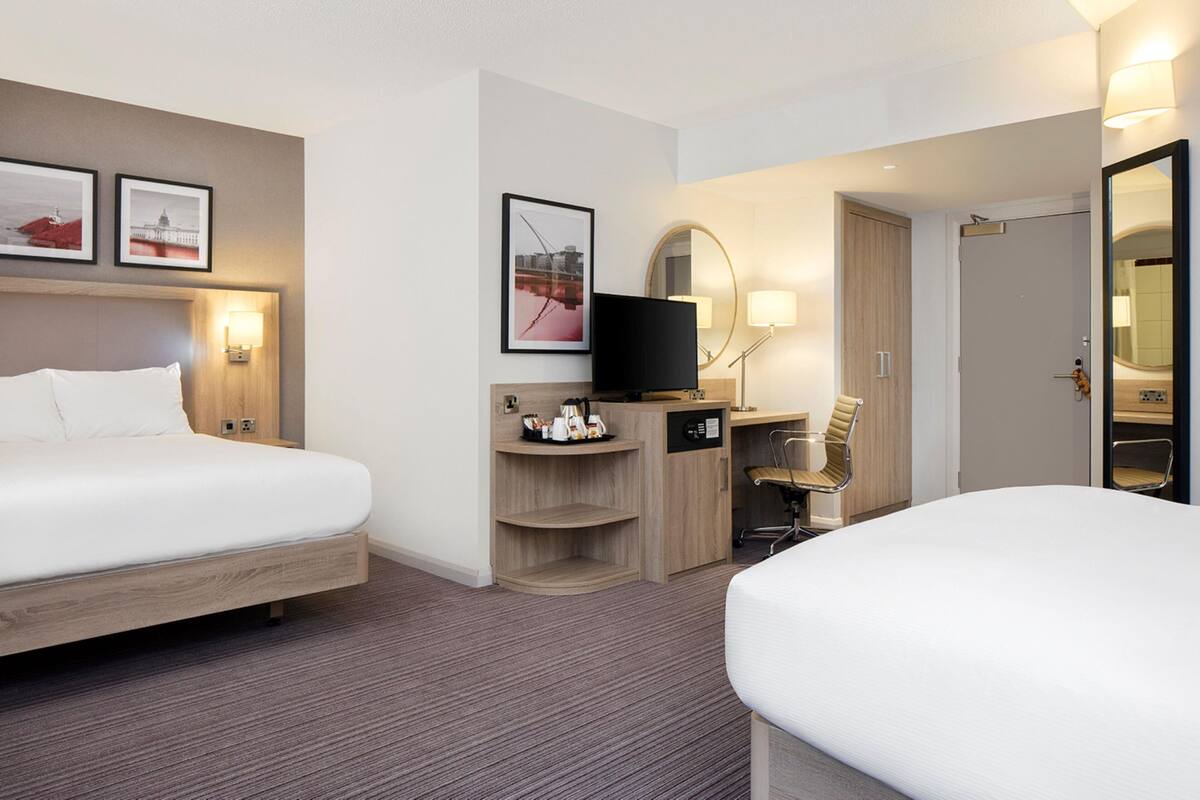 A hotel room with two beds, a desk with a flat-screen TV, a chair, and a mirror.