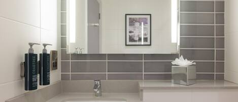 A modern bathroom with a large mirror, a sink, and two bottles of Crabtree soap.