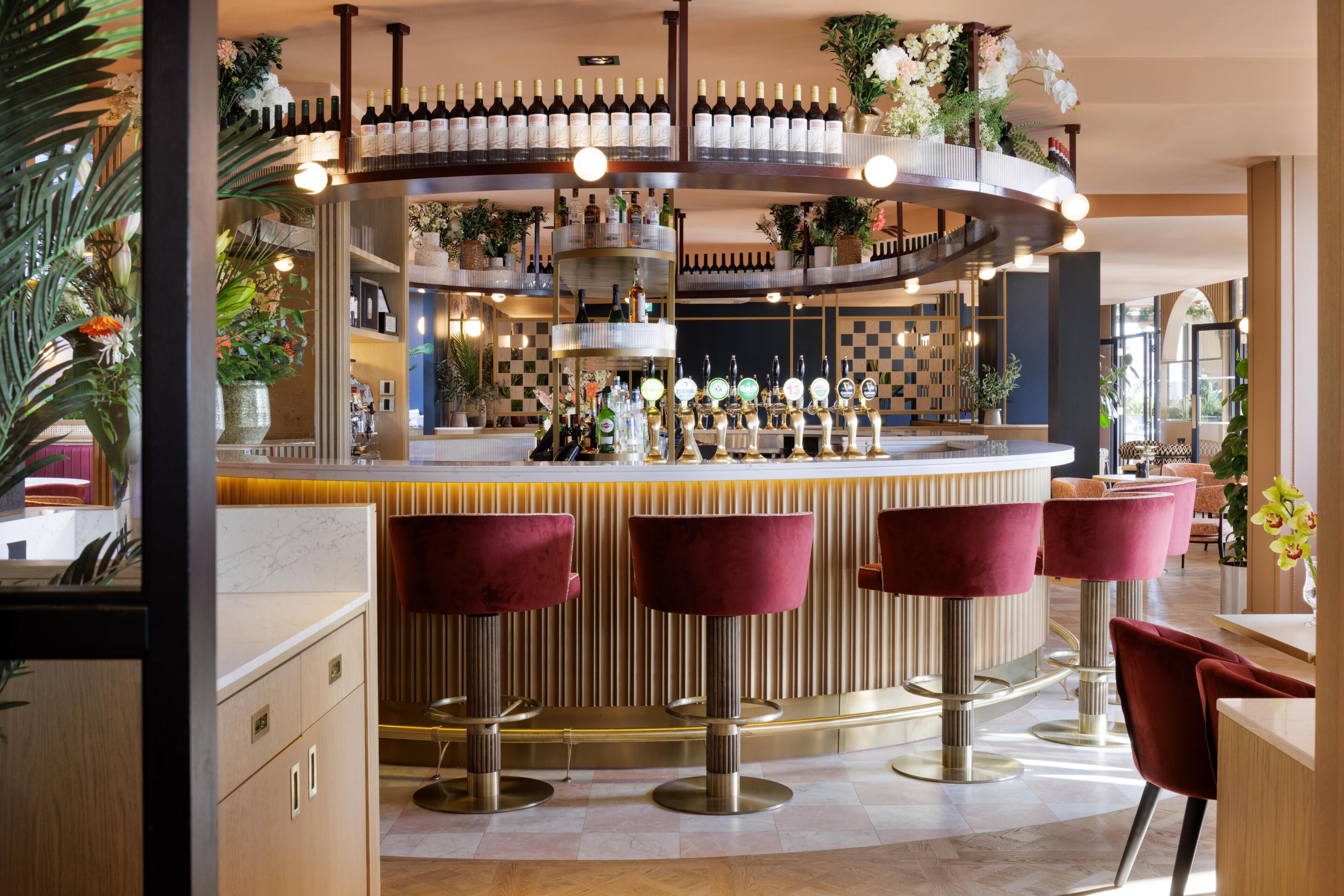 A bar area with a circular bar, multiple stools, and a variety of bottles.