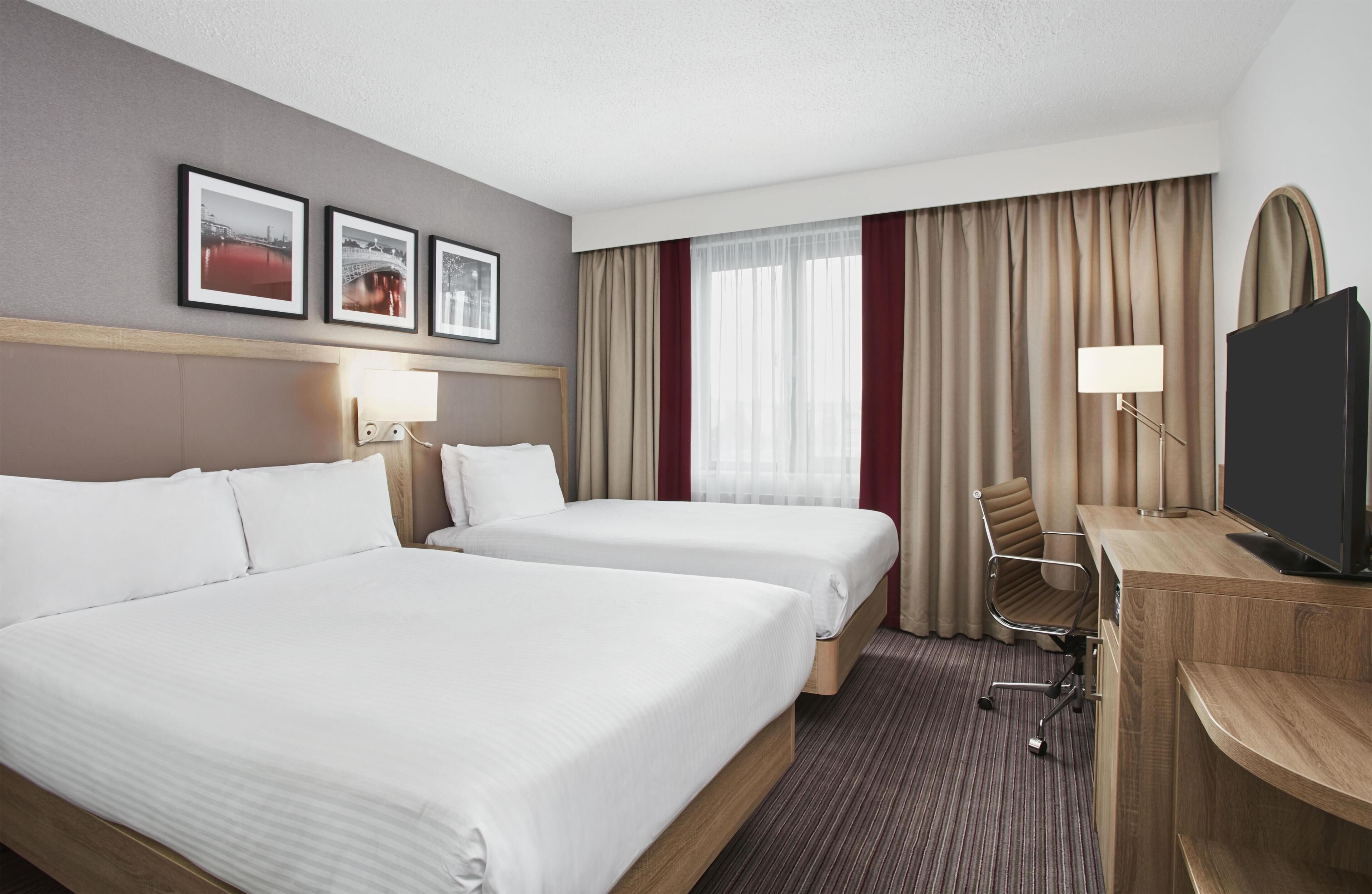A hotel room with two beds, a desk with a TV, a chair, and framed pictures on the wall.