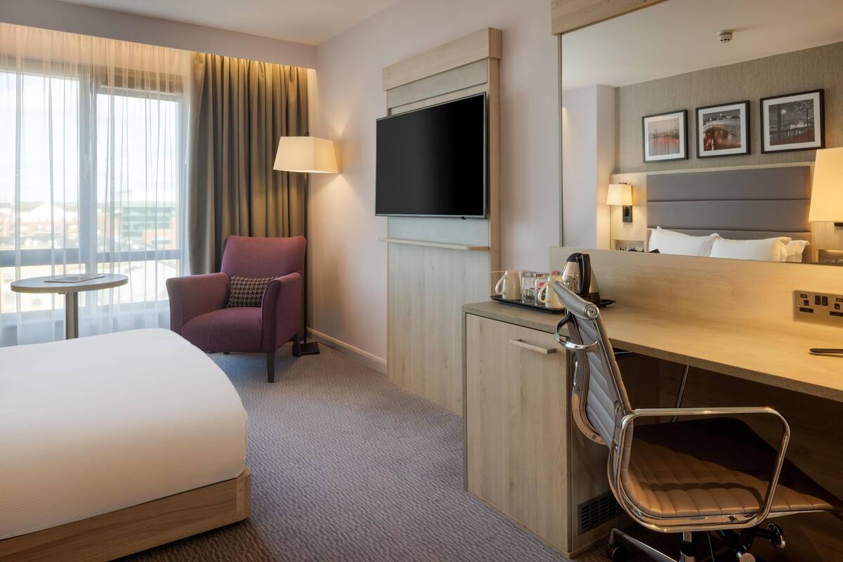 A hotel room with a bed, a desk, a chair, a television, and a window with curtains.