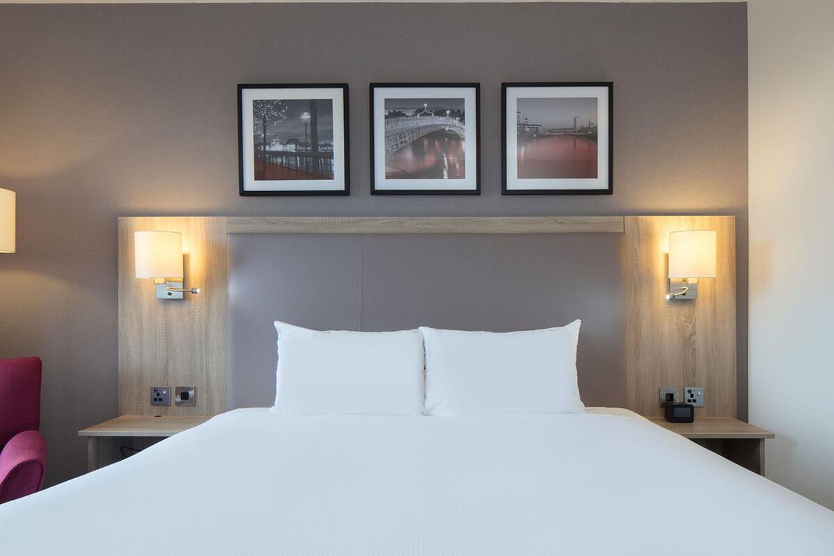 A hotel room with a large bed, two bedside tables, a headboard, and three framed pictures on the wall.