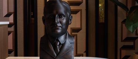 A bust of Honey Fitz on a marble table with a geometric patterned wall in the background.