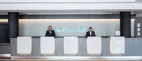 A reception desk with three counters, a city skyline mural, and a polished marble floor.