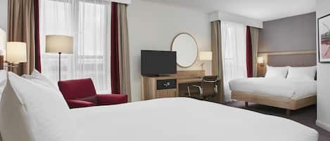 Una habitación de hotel con una cama grande, un escritorio con televisión, una silla y una mesita de noche.