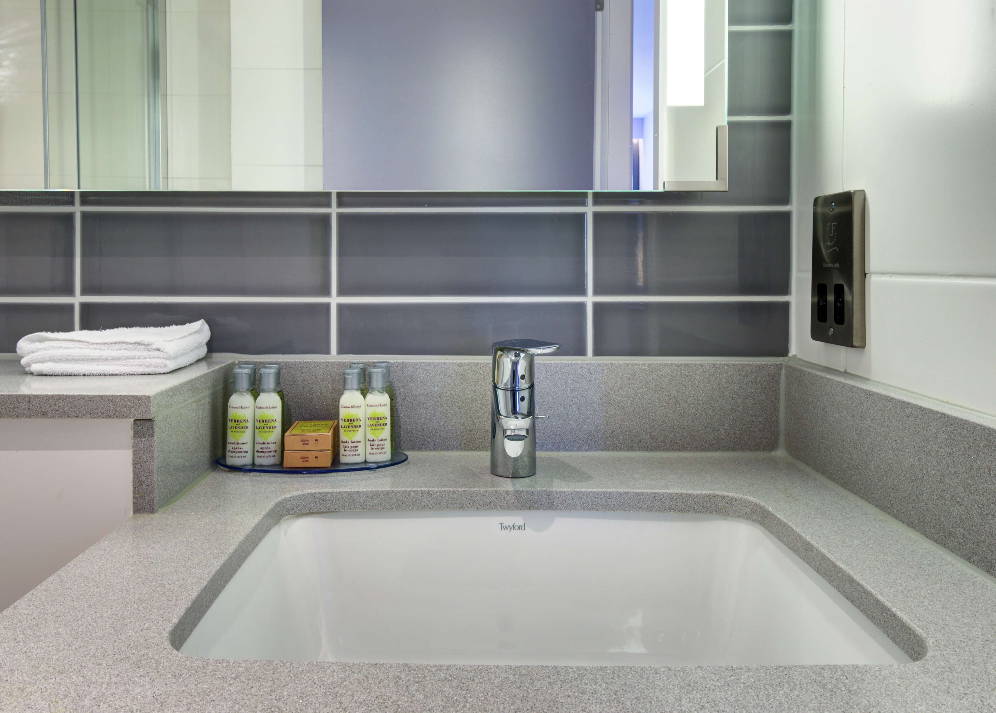 Une salle de bain moderne avec un grand lavabo, un porte-serviettes et trois bouteilles de lotion pour le corps.