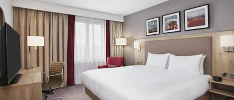 A hotel room with a large bed, a desk, a chair, and two wall-mounted lamps.