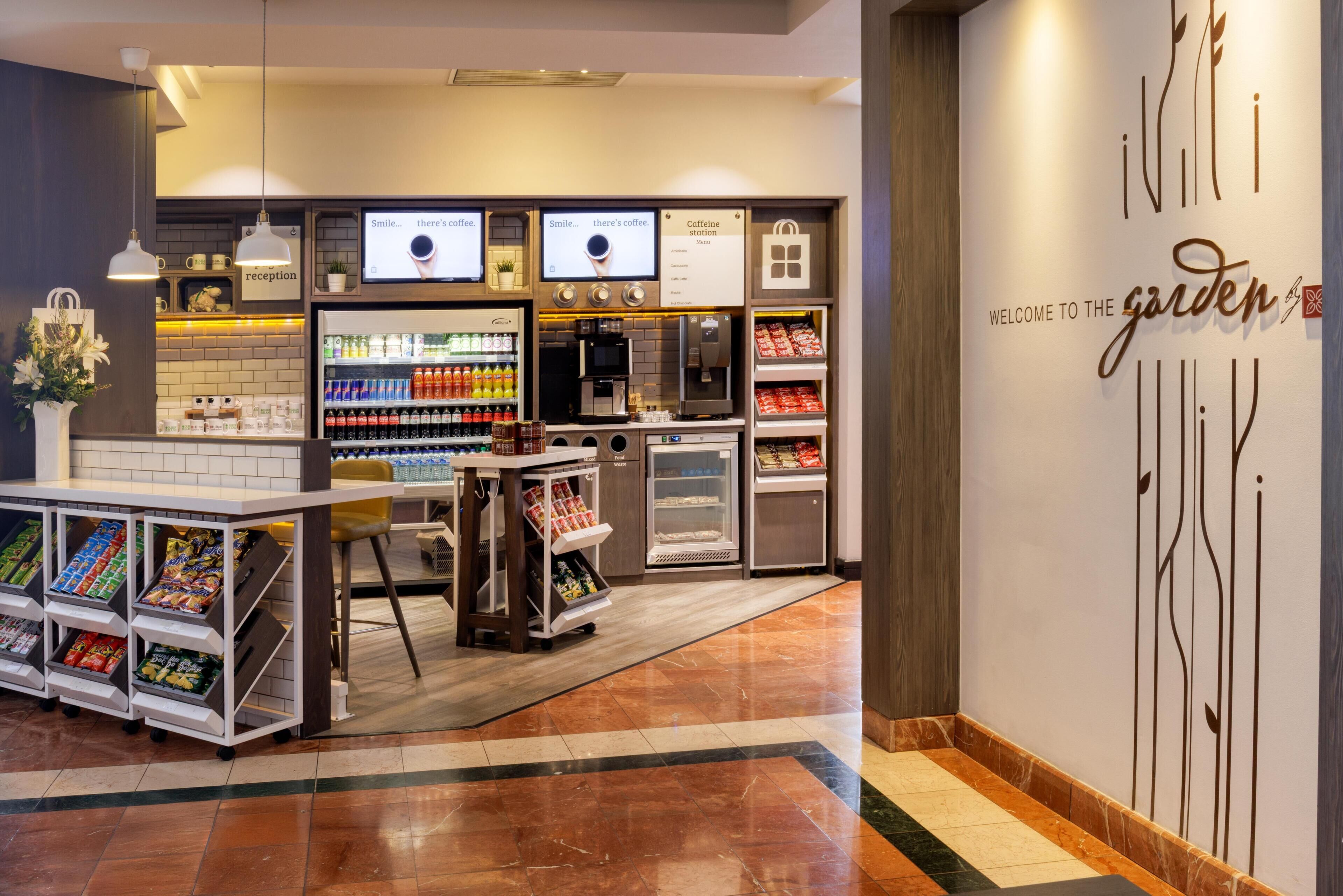 A modern coffee shop interior with a reception desk, coffee machines, and a variety of beverages.
