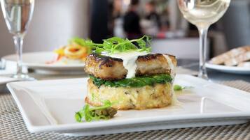A plated dish with a creamy sauce, greens, and a piece of meat, accompanied by a glass of white wine.