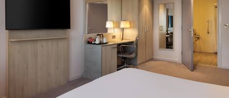 Habitación de hotel con cama, televisión, escritorio con silla, espejo y puerta que da a un baño.
