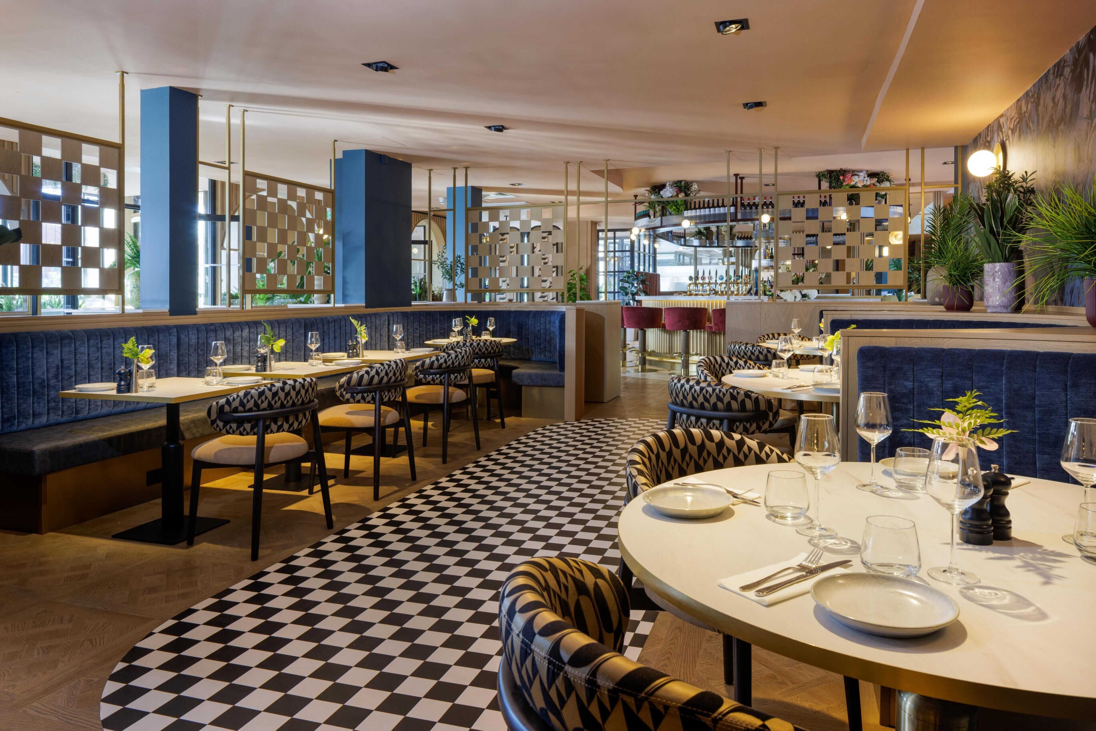 A restaurant with checkered flooring, round tables, and booths.