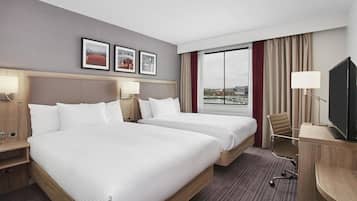 Habitación de hotel con dos camas, televisión, escritorio y ventana con vista a la ciudad.