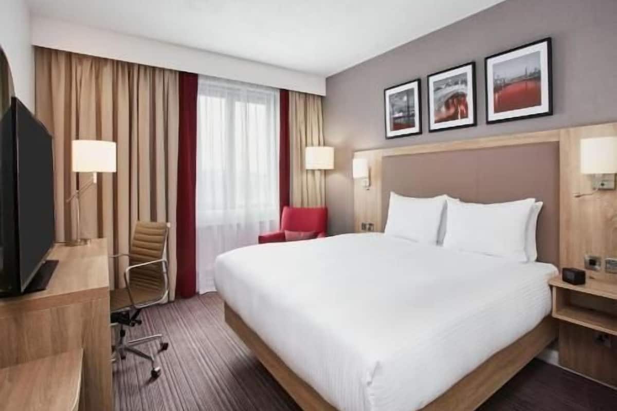 A hotel room with a large bed, a desk, a chair, a TV, and a window with curtains.