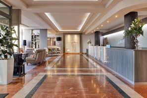 Eine Hotelhalle mit Empfangsschalter, Sitzgelegenheiten und einer großen Pflanze.