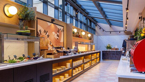 A modern hotel lobby with a long reception desk, a glass ceiling, and a view of the sky. - Hilton Garden Inn Dublin City Centre (Dublin)