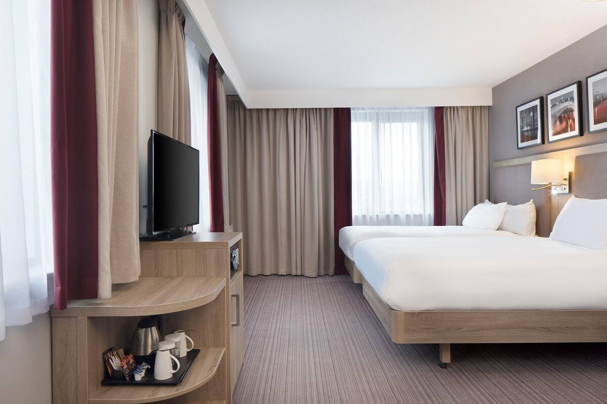 A hotel room with a bed, a TV, a coffee maker, and a tray with breakfast items.